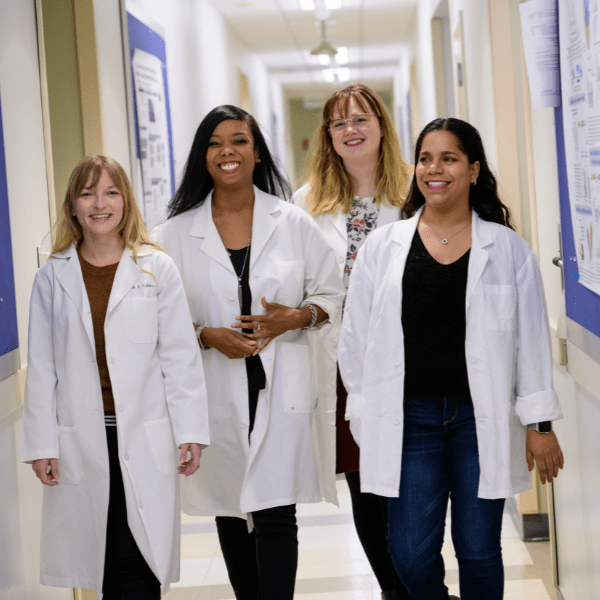Group of four women in lab coats walking down a hallway