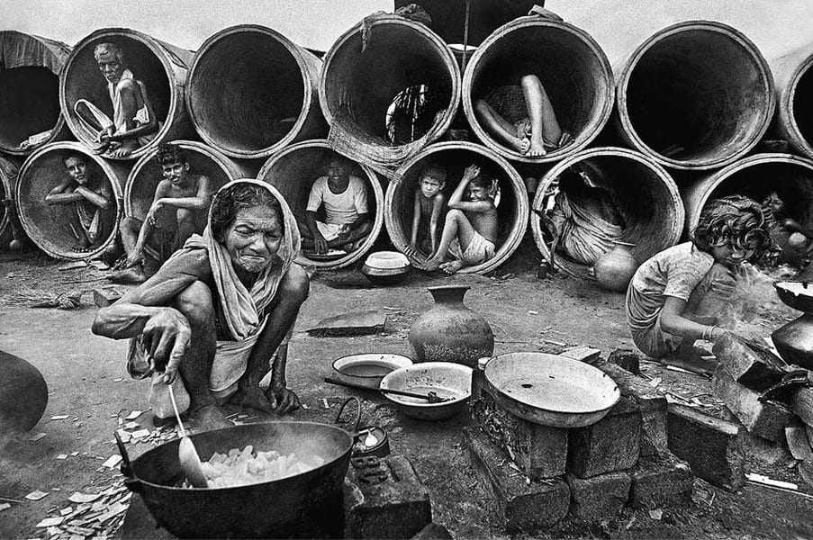 Refugees sit in cement pipes while other refugees cook.