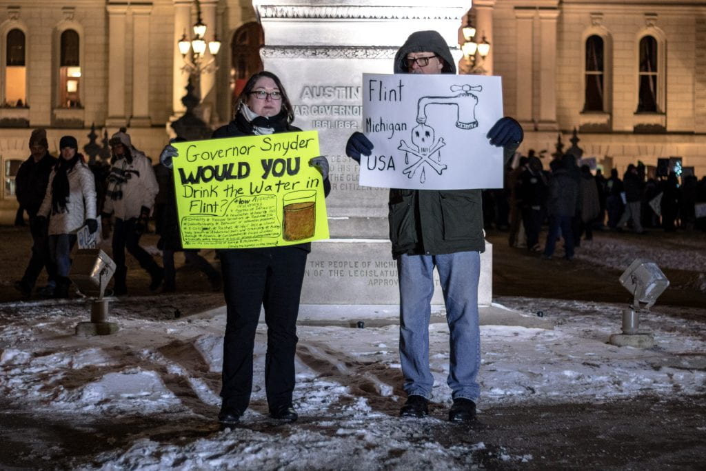 Two protesters hold signs decrying the lack of clean water in Flint