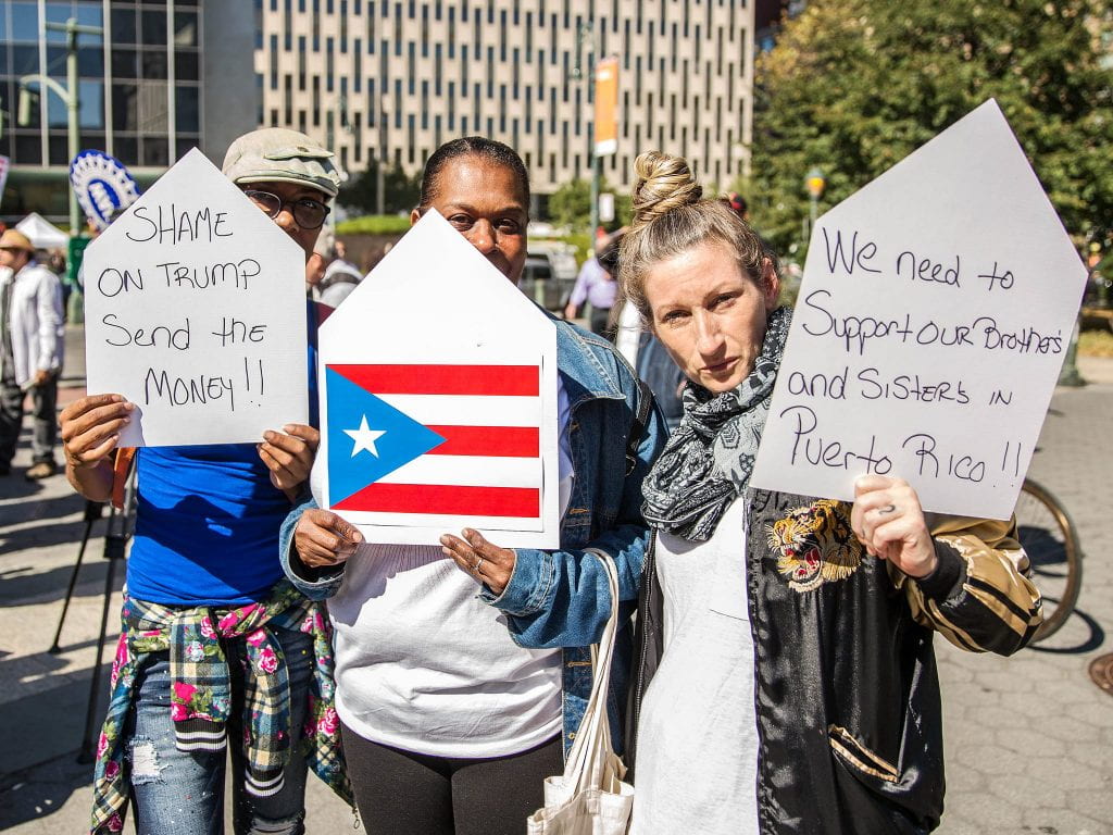 Three people hold signs at a protest supporting Puerto Rico. 