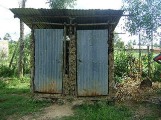 a picture of a traditional pit latrine, which looks like a very small building with a tin roof and two tin doors