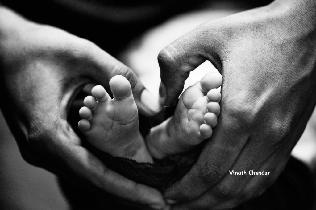 Tiny baby feet are cradled by hands in a heart shape.