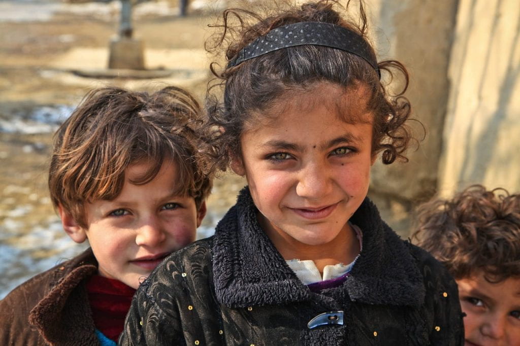 Three curly haired Afghan kids look up to the camera