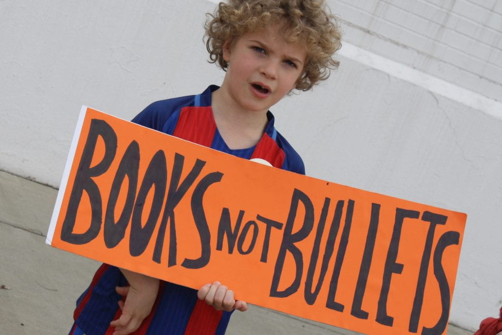 a picture of a boy holding a sign which reads "books not bullets" during the March for Our Lives