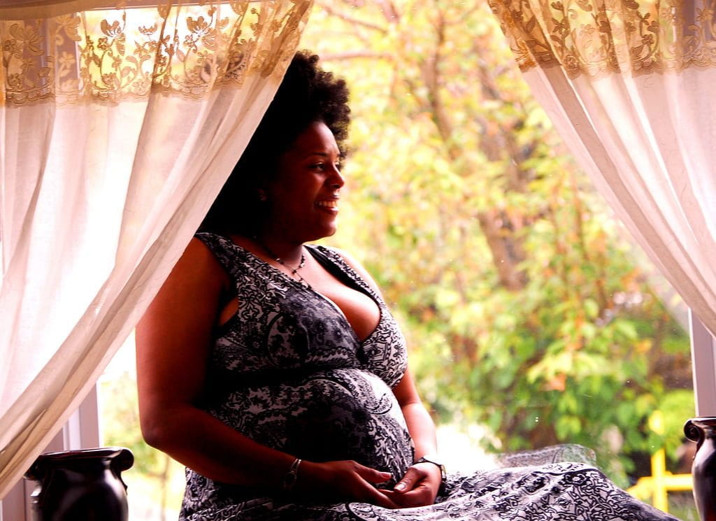 a pregnant Black woman sitting on a windowsill