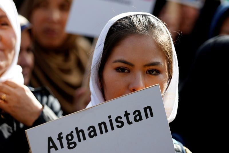 A woman with a white headscarf holding a poster that says "Afghanistan"