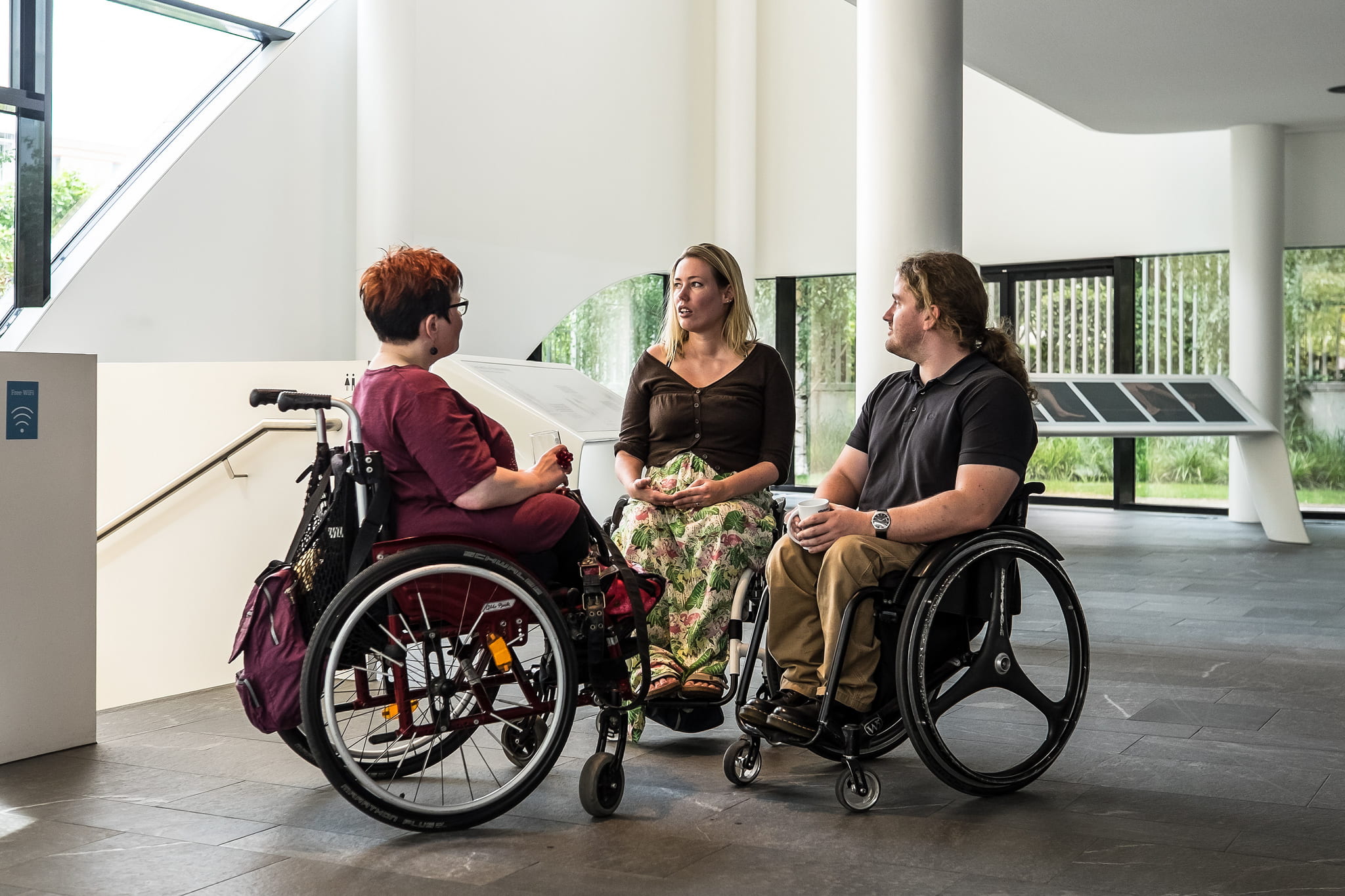 Three people in wheelchairs face each other while talking.