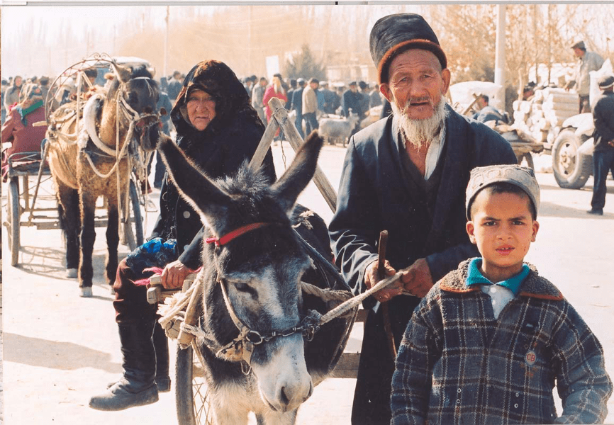 A pair of Uyghur elders lead a donkey and boy across a Chinese marketplace