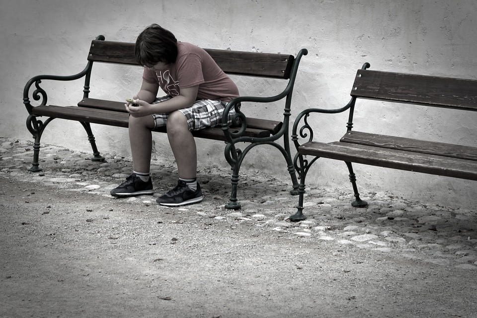 a picture of a young boy sitting alone on a park bench