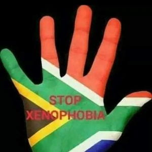 A hand painted with South African flag that says "Stop Xenophobia"