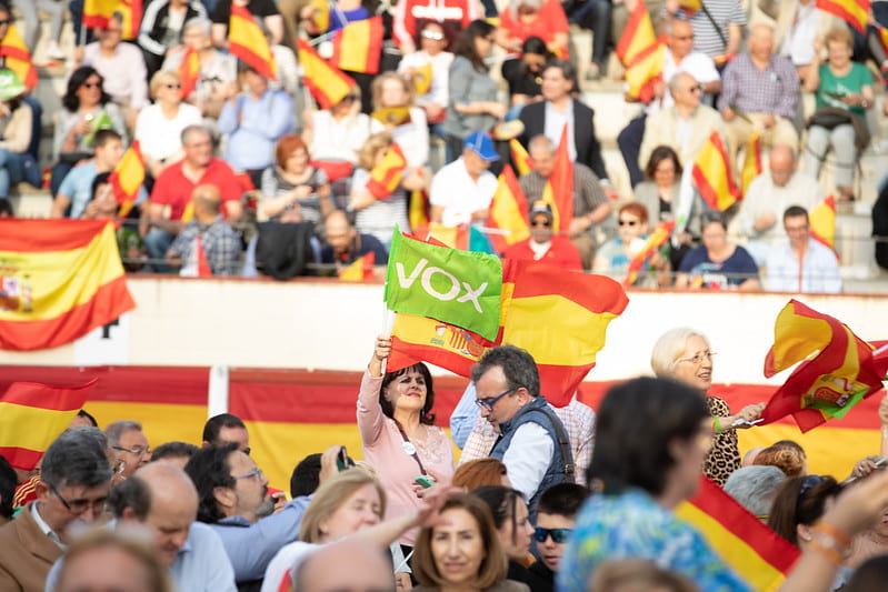 A woman waves a Spanish flag and a Vox party flag at a rally.