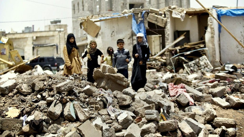 Children standing over ruins in Yemen.