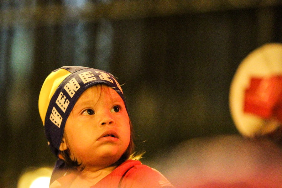 Child wears hat that says Venezuela on it and stares off into the distance.