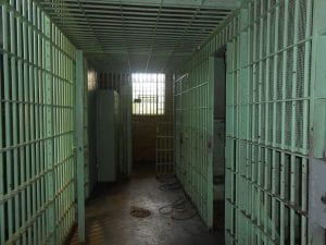 Inside of a jail, a dark hallway with green jail cells on either side