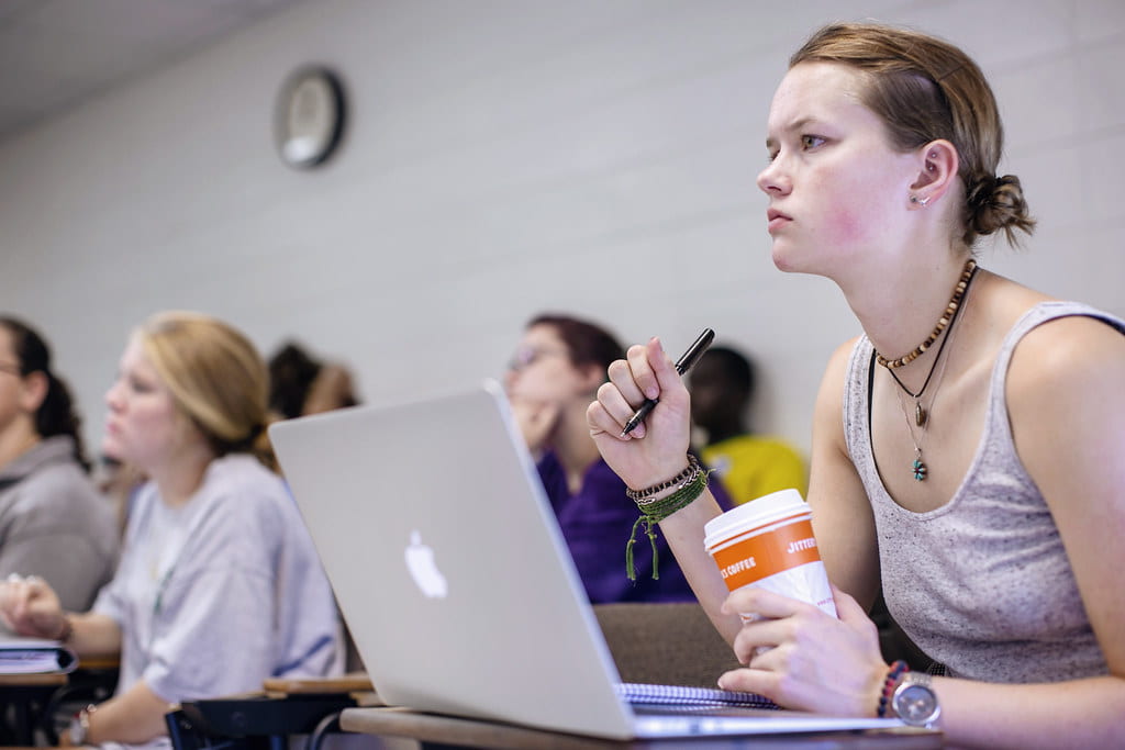 A girl in front of a laptop in a college classroom