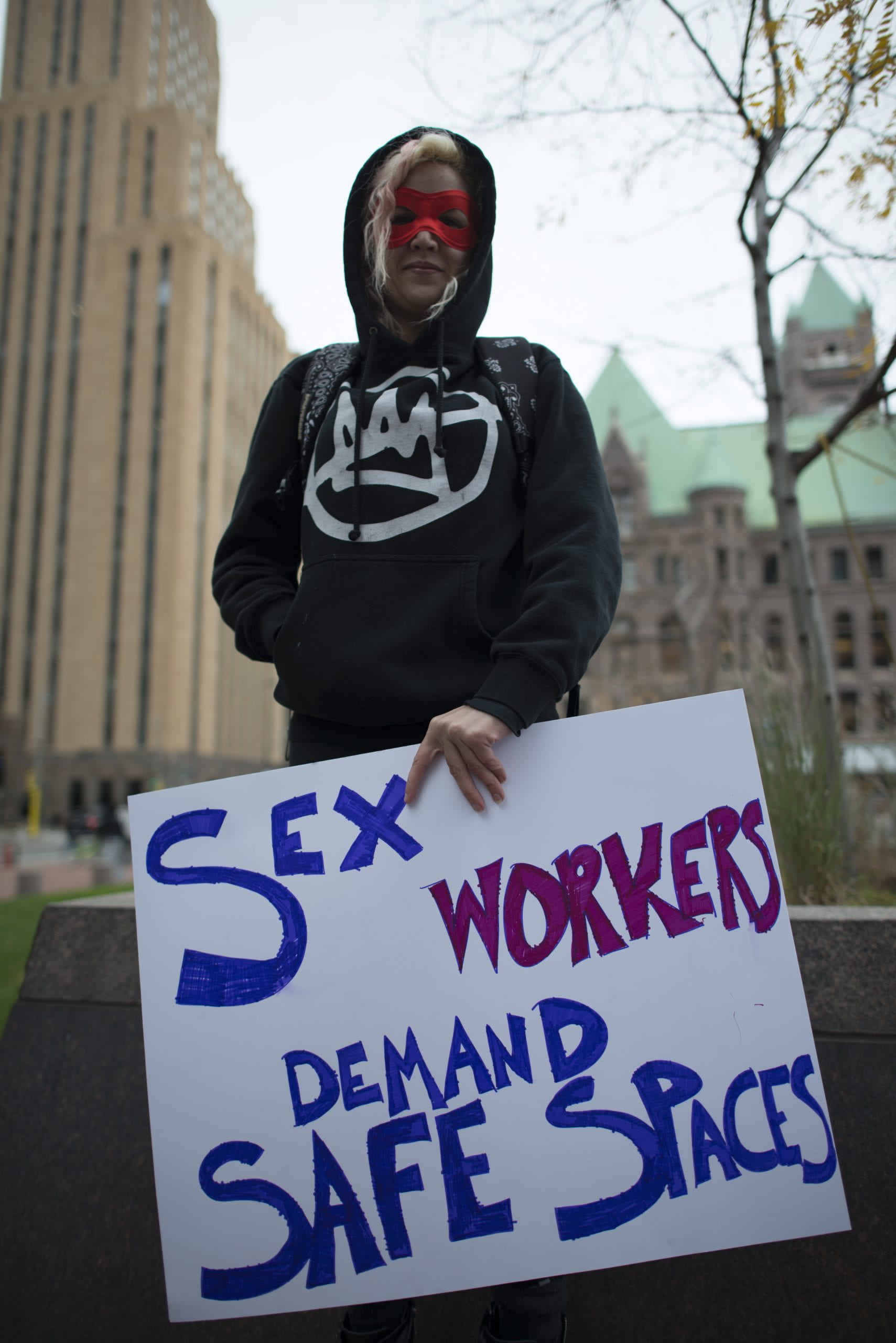 Woman holding poster reaing "Sex Workers Demand Safe Spaces"