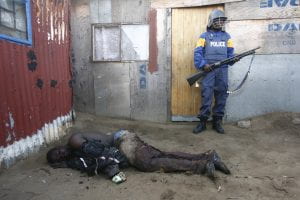 An injured African Immigrant lying face down on the ground with a armed policeman standing over him. 
