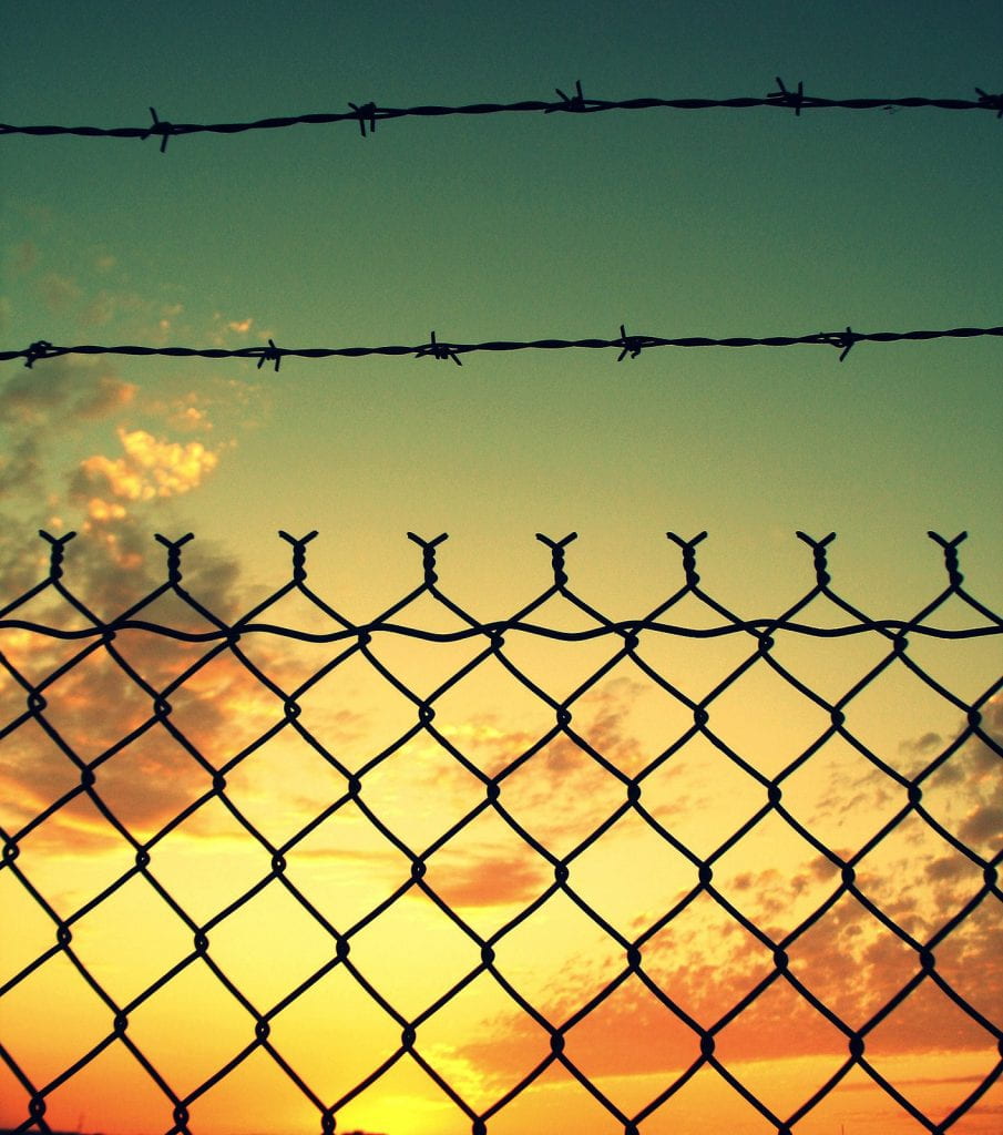a picture of a sunset through a barred wire fence