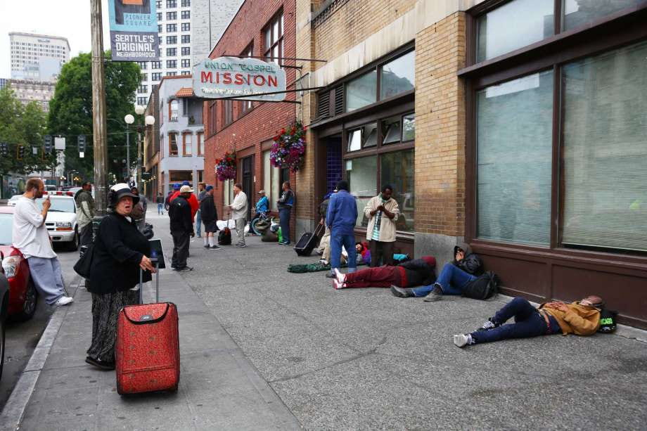 Picture of a homeless shelter with people standing around and lying down, waiting for a meal and a bed