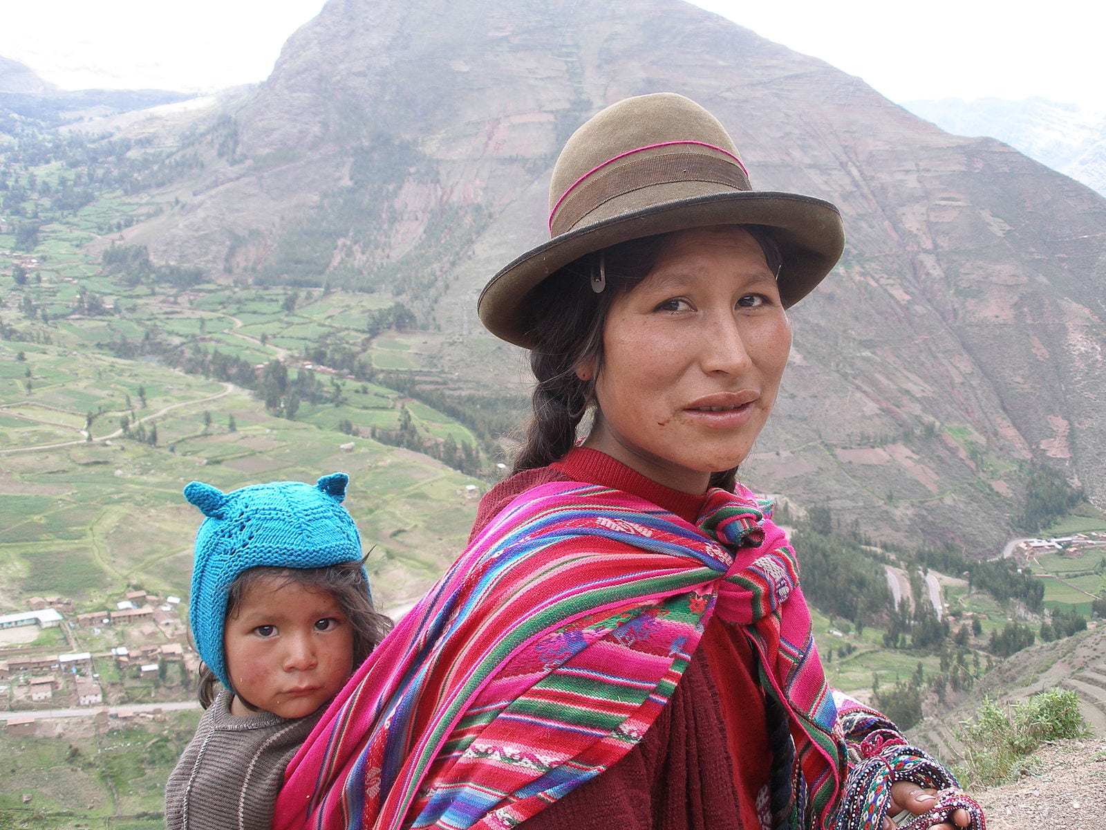 Indigenous Peruvian woman carrying her child on her back with mountains in the background