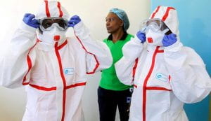 Two individuals in hazmat suits stand in front of a Kenyan woman as the first cases of Covid-19 are diagnosed