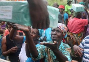 A poor woman in traditional African garb holds out her hands for a relief package