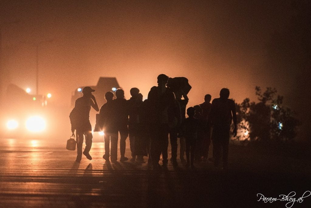 Migrant workers walking on the shoulder of a highway during the nighttime.