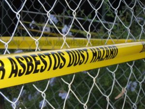 A fence with yellow caution tape that says Asbestos Dust Hazard