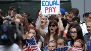 Photo of a protest with woman holding sign that reads "Equal Pay"