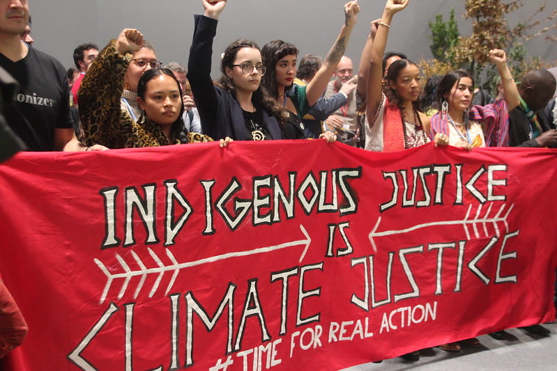 A group of young protestors holding a red banner reading "indigenous justice is climate justice."