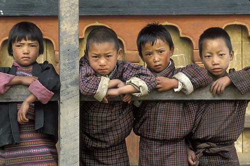 Bhutanese children in traditional attire, leaning over a balcony