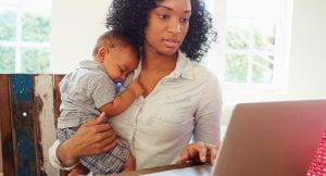 Woman working on a laptop while holding a baby