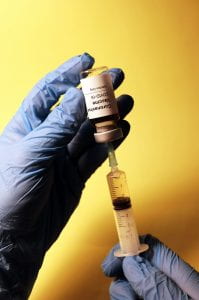 Gloved hand pulling the liquid of a bottle labeled COVID Vaccine into a syringe meant to vaccinate people.