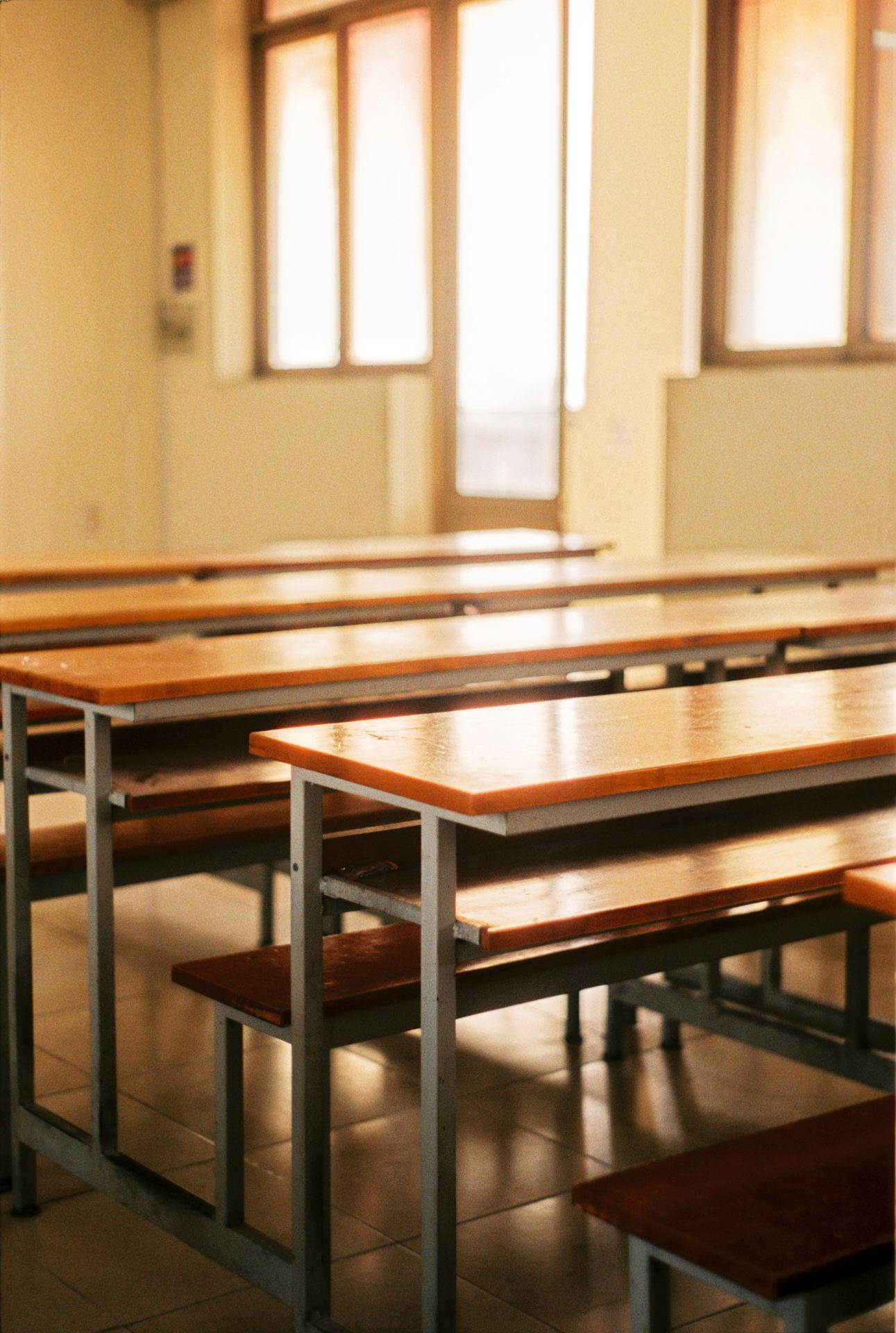 The image depicts rows of wooden benches in a well-lit classroom. 