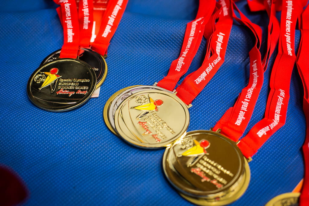 The image displays gold medals stacked in pairs. Engraved on the medals is writing and a logo signifying the Special Olympics. 