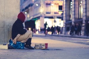 Photo of a man sitting on  street with sign asking  for money