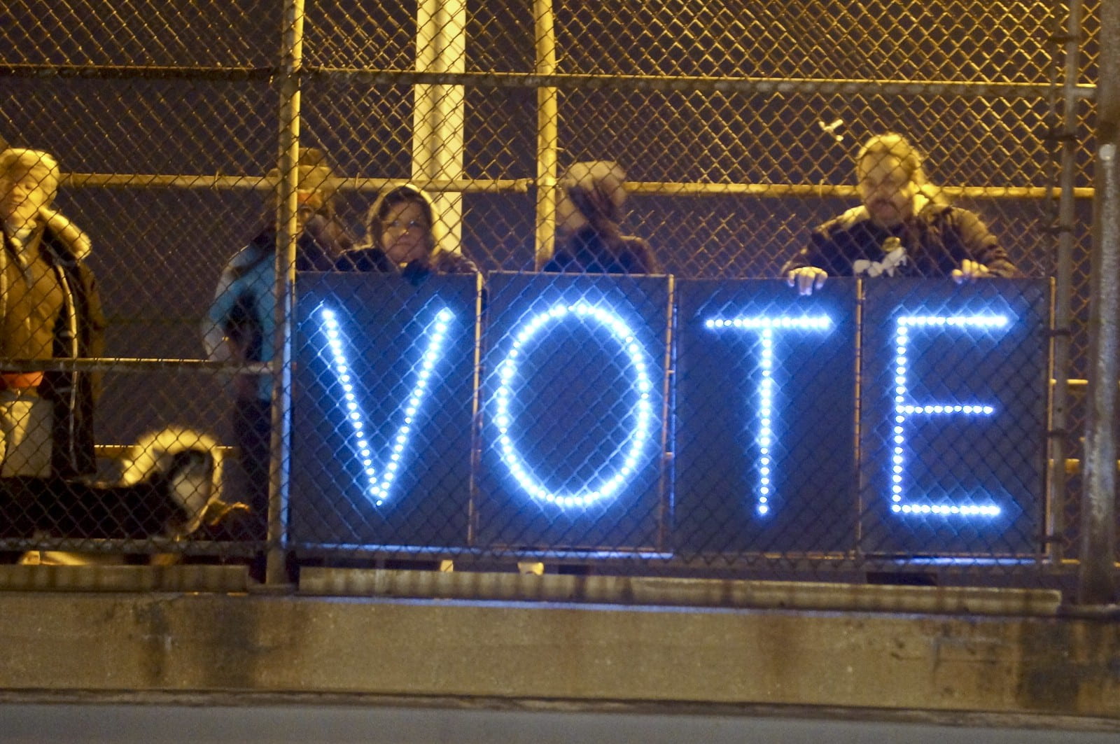 People holding up a sign that says "VOTE" in neon letters