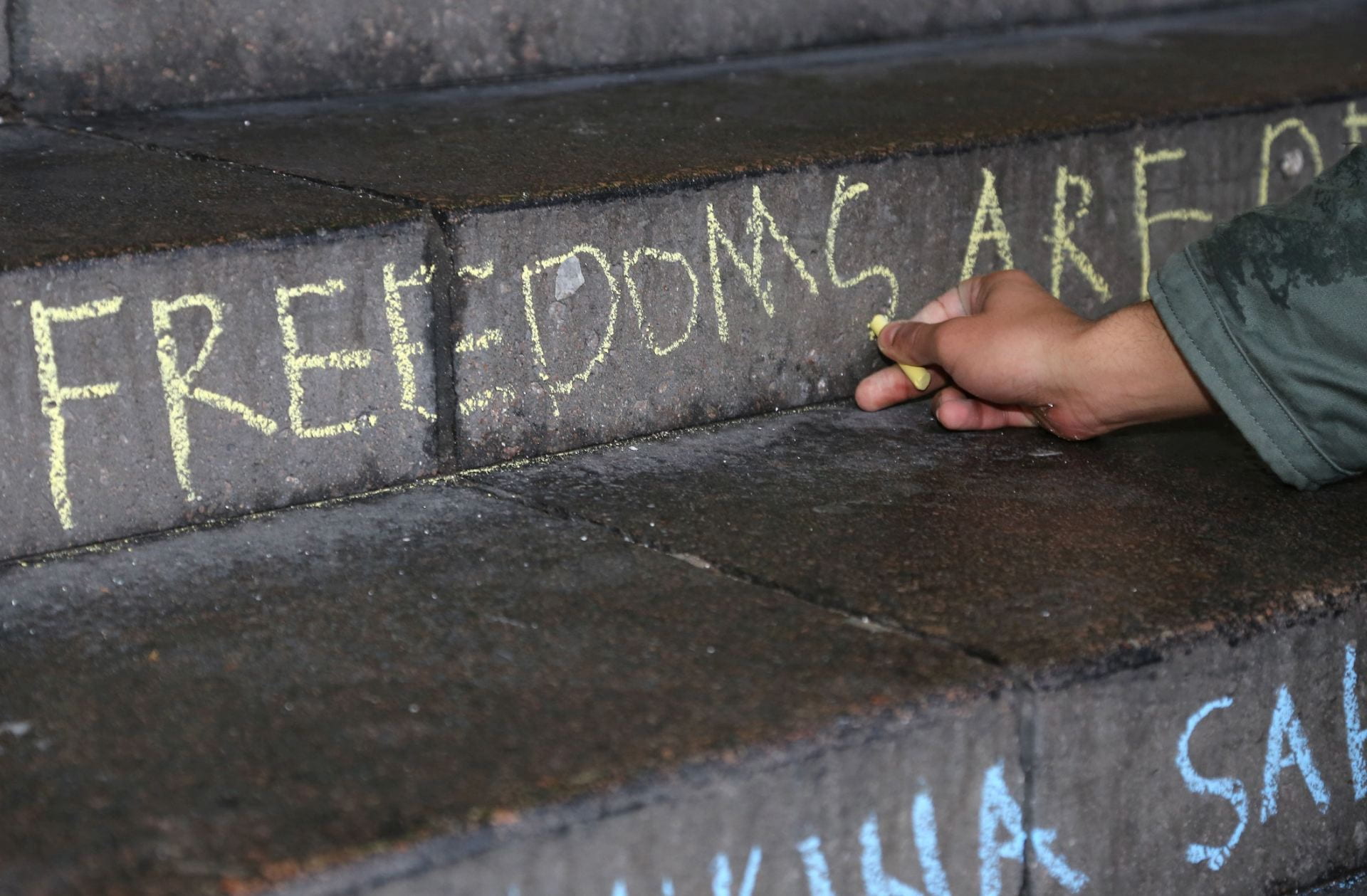Image shows a person writing the word freedoms using chalk on a concrete staircase.
