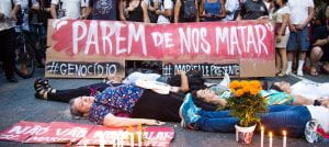 Photo of women lying down in protest in front of a sign that reads "Parem de nos matar"