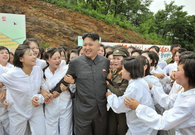 Kim Jong-Un smiles amongst a group of women. They are all wearing white uniforms, crying out, and grabbing onto Kim in adoration.