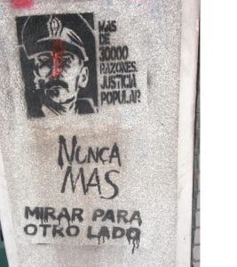 Spray painted image of a general with crossed-out eyes on a wall. The words “More than 30,000 reasons for popular justice. Never again look the other way" are painted beside the images.