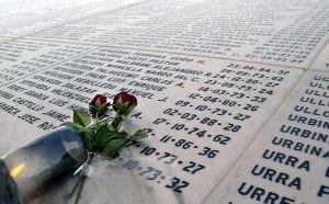 Flowers resting atop white marble covered with names and dates. 