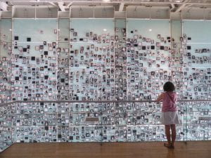 Photo from behind a person in front of a wall of pictures of people.