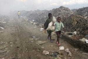 Two children in tattered clothes walk through a trash dump