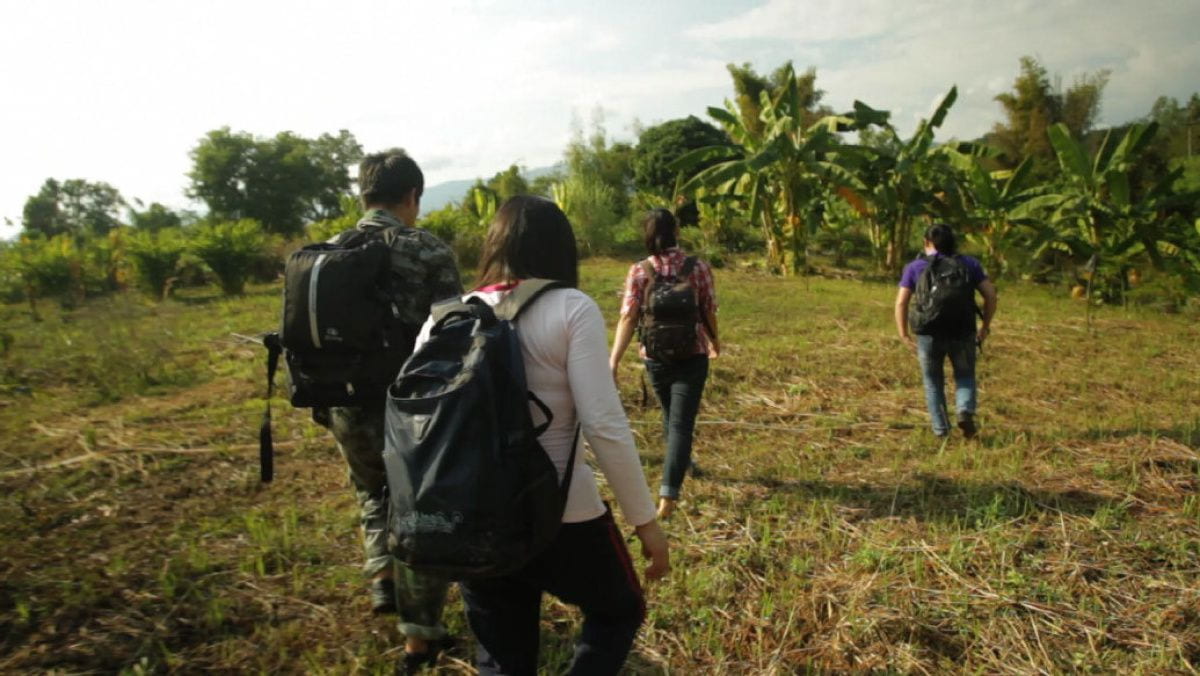 Four refugees wearing backpacks walk through a field to safety.