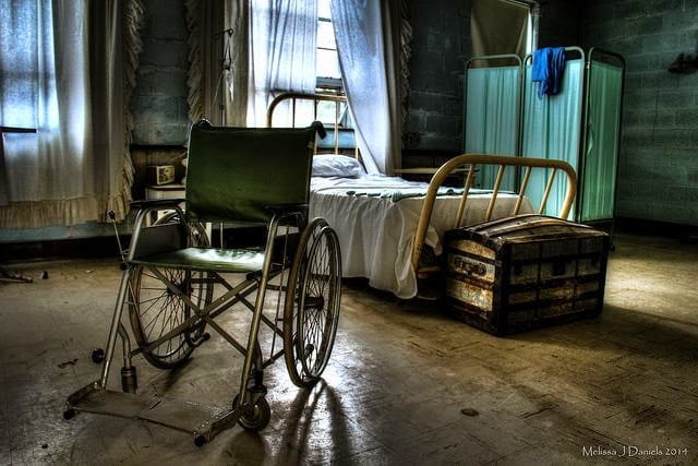 An image depicting an asylum, where people with disabilities were forcibly committed. In this image, there is a bed, and a wheelchair in the room big enough for one person, but many facilities were not as fortunately funded or furnished.