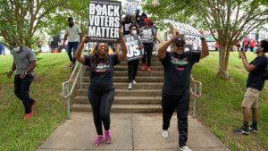 An image of people holding signs in the air that read “Black Voters Matter” as they come down a set of stairs. 