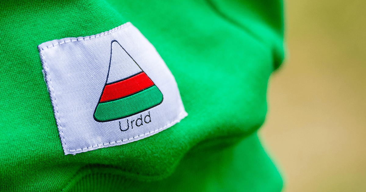 Image shows a green sweatshirt with a white patch sewn on showing the Urdd logo.
