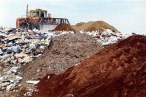 A landfill with dirt to the right and general waste to the left. A large tractor can be seen in the background.