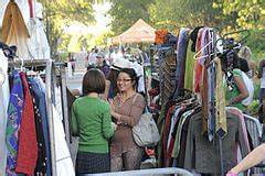 Two women talking to each other. They are standing between two clothing rails on the street at a secondhand clothing sale.